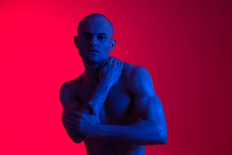 Portrait of a confident man in dramatic lighting, showcasing strong physique and captivating expression, highlighting the interplay of shades and shadows.