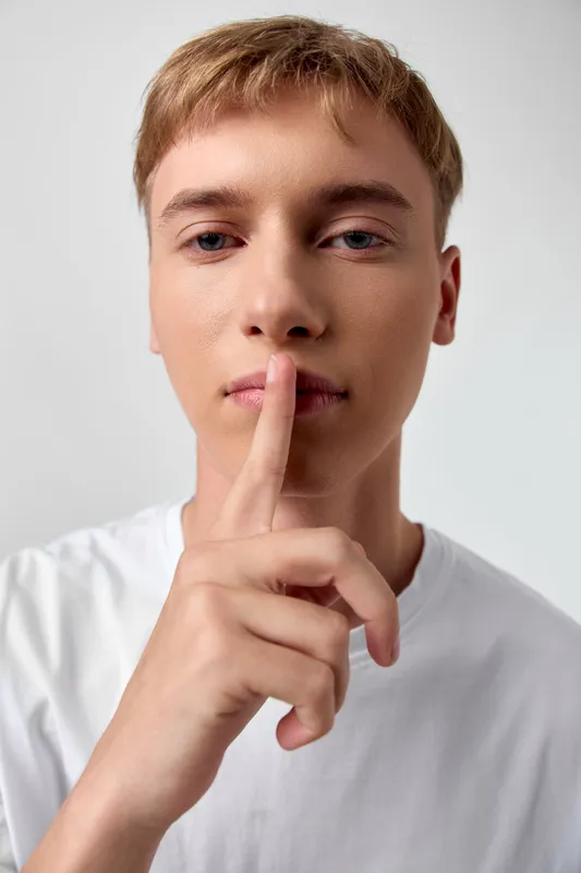Silence, shh, quiet, secret, finger, lips, gesture, communication, hush, expression captured in a simple studio scene with a focused mood and subtle restraint