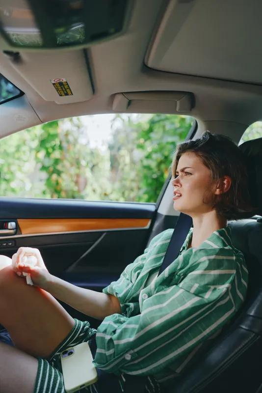 A woman sits in a car with a seatbelt on, wearing a green striped shirt, sunlight filtering through the window, capturing a candid moment of calm travel.