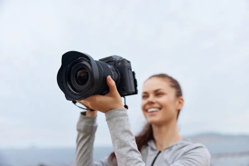 Young woman with a camera capturing moments outdoors, showcasing joy and creativity in a gray landscape, perfect for photography enthusiasts and social media content