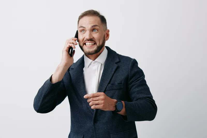 Portrait of a business professional man on a call, displaying tense yet confident emotion, isolated on a clean, solid light gray background, in a modern corporate setting.