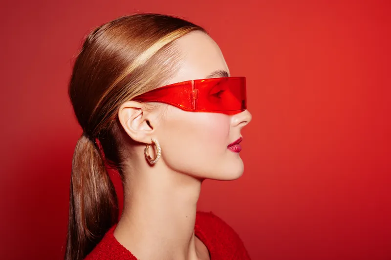 Profile of a stylish woman with red sunglasses and red lipstick against a red background. Concept of fashion, beauty, modern style, and confident attitude in studio lighting.