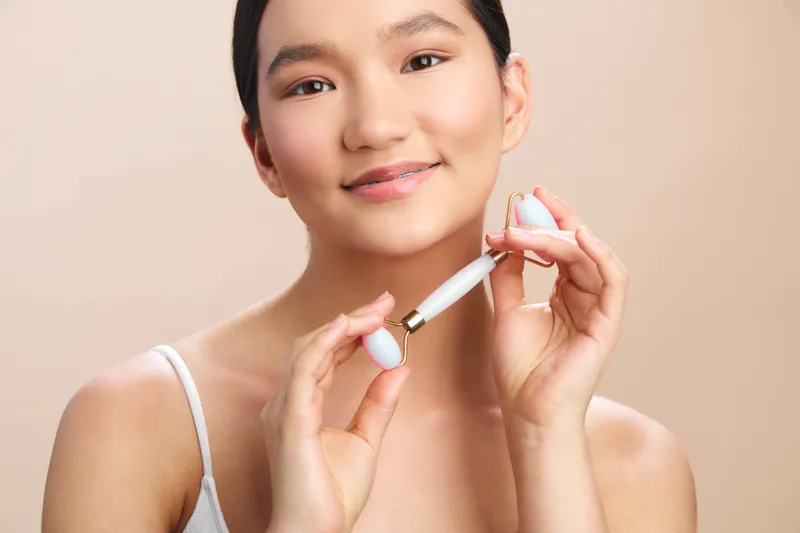 asian woman uses a skincare device in a bright modern setting, smiling softly as she demonstrates a routine, conveying calm wellness and self care in a sleek environment.