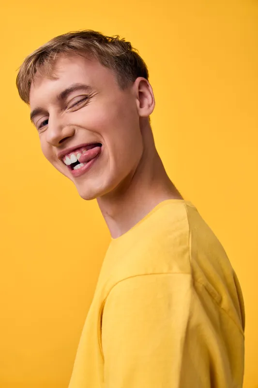 Smiling man, yellow shirt, funny grin, crooked teeth, playful expression, studio scene, bright backdrop, energetic mood, bold color, candid and lighthearted moment in a controlled setting