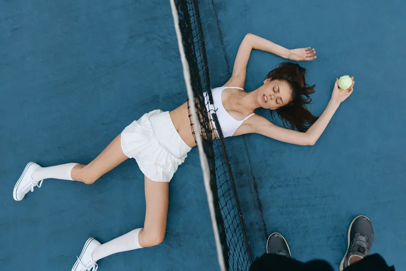 A young female tennis player relaxed on a blue court, wearing a white sports outfit, showcasing determination and passion for the sport, with a tennis ball