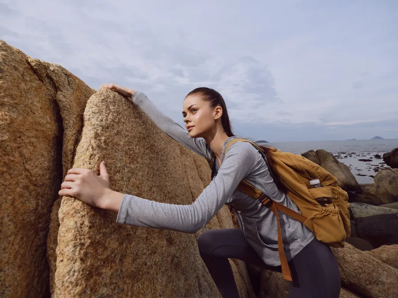 Young woman hiking on rocky terrain, showcasing determination and adventure in an outdoor setting, earthy tones with a natural background