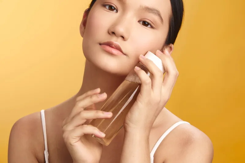 asian woman applies skincare product in a bright minimal studio, calm expression, soft lighting conveys beauty and wellness, modern self care scene with personal care routine and radiant complexion.