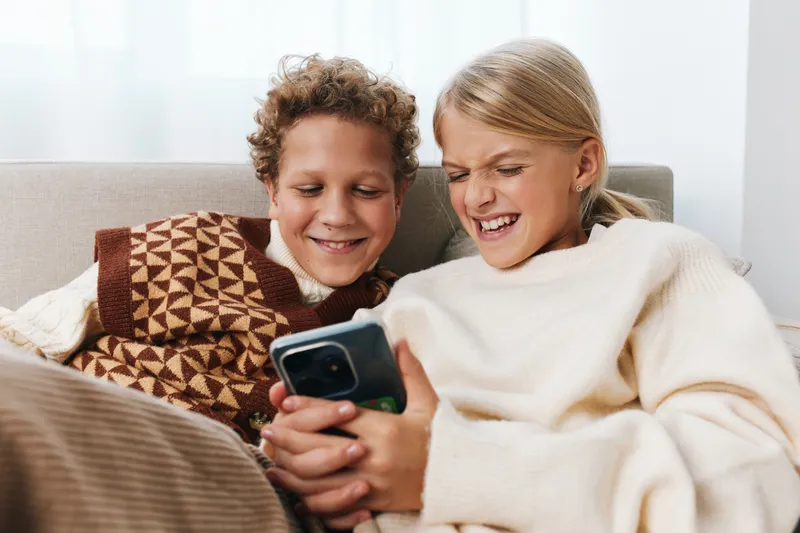 Authentic scene of siblings sharing playful moments at home, capturing lifestyle wonder and school inspired curiosity as they explore a mobile device together.