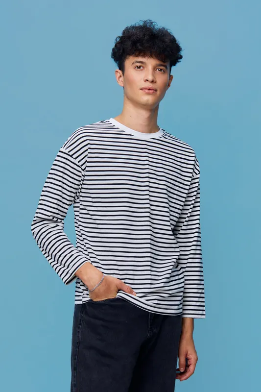 Young man in a striped long-sleeve shirt posing confidently against a solid light blue background, casual style with relaxed posture and natural expression.