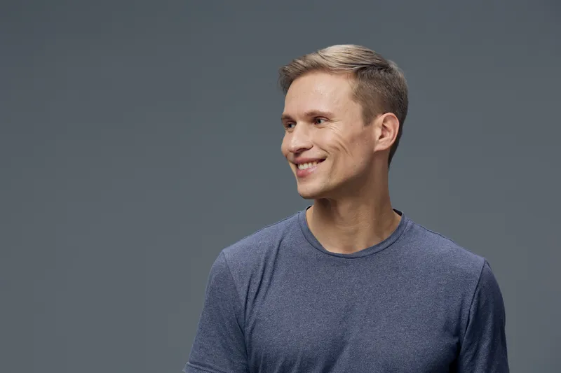 Smiling man in casual blue shirt looking away against plain gray background, expressing happiness, friendliness, confidence, relaxed posture, natural expression, indoor studio shot. People lifestyle c