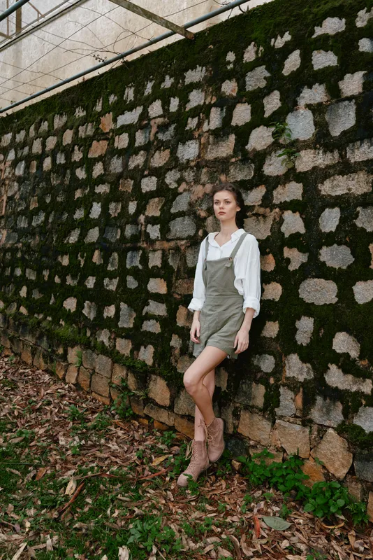 Young woman in stylish overalls against a textured stone wall, showcasing a casual look and natural beauty in an outdoor setting
