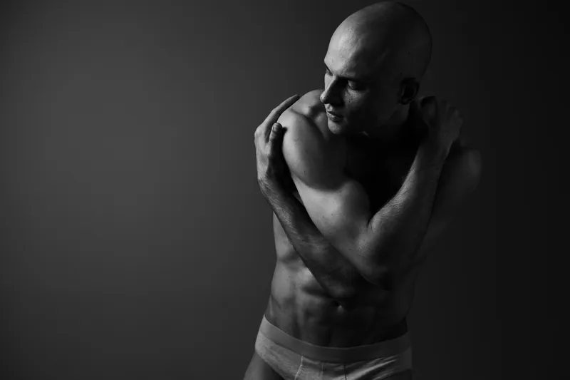 Black and white image of a man posing creatively with his arms, showcasing strength and emotion in a dramatic light setting.