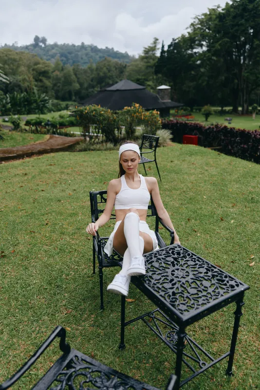 Young woman in sporty attire relaxing outdoors on a sunny day, showcasing a peaceful moment amidst nature with a vibrant green background