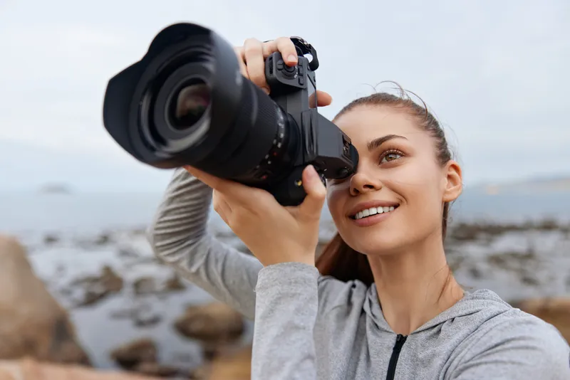 Young woman photographer capturing stunning nature scenery with a DSLR camera on a rocky shore, showcasing determination and passion for photography