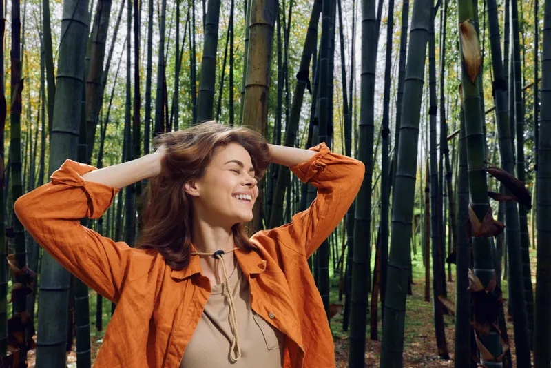 Woman bamboo forest smile nature portrait outdoors happiness young woman in orange jacket enjoying a peaceful walk among tall bamboo stalks, eyes closed and hands behind head.