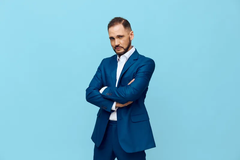 A confident business professional stands isolated against a vibrant blue background, arms crossed, projecting focus, determination, and readiness for strategy, leadership, and decisive action.
