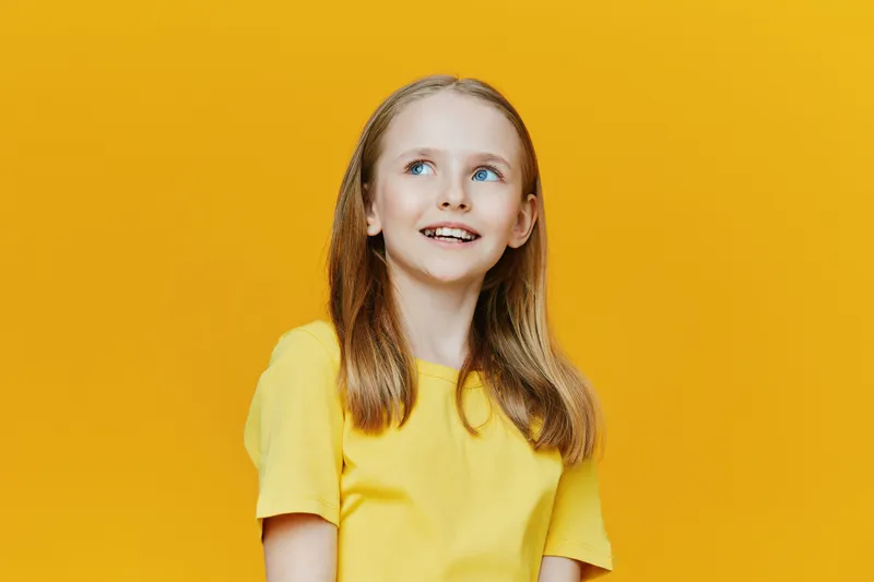 Smiling girl wearing a yellow shirt against a bright yellow background, showcasing happiness and youthful energy in a vibrant and cheerful setting, ideal for concepts of joy and childhood