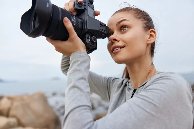 Young female photographer capturing nature images with a DSLR camera, dressed in casual sporty clothing, showcasing joy and creativity by the sea