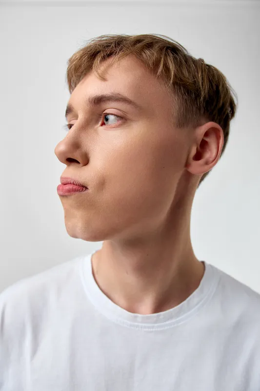 Thinking man in profile wearing a white tee, captured in a clean studio setting, conveying contemplation and calm, with soft lighting and simple background suitable for fashion, lifestyle, and