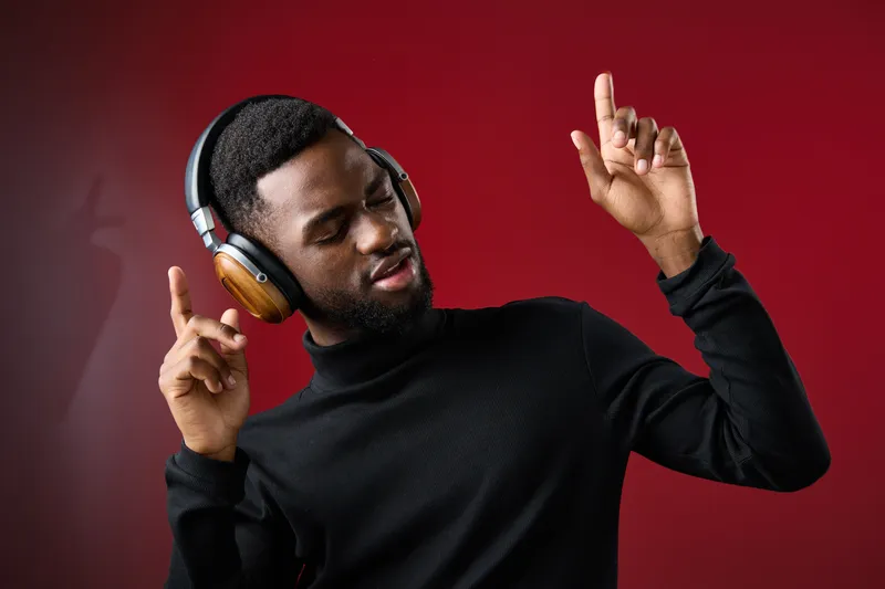 Young Black man enjoying music with headphones, showing joy and energy against a red background in a stylish black outfit, perfect for modern lifestyle concepts