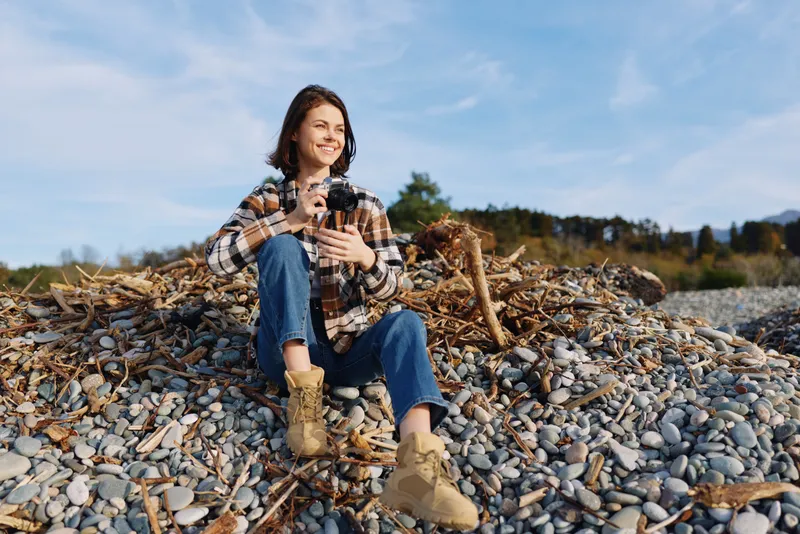 woman outdoor casual portrait rocky beach nature smiling relaxed on a pebble shoreline with plaid shirt and boots capturing a serene moment in natural light