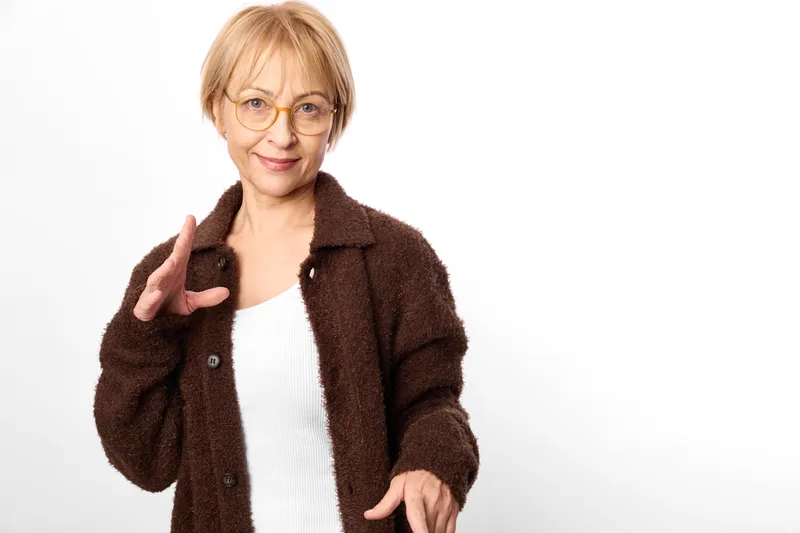 Elderly woman with glasses and brown coat in studio white background isolated view confident gesture with hand pointing senior portrait
