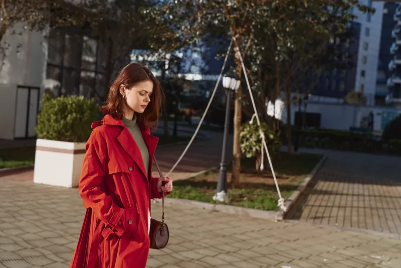 A woman in a red coat walks through an urban outdoor plaza, daytime light, contemporary cityscape, stylish street fashion shot with a candid mood