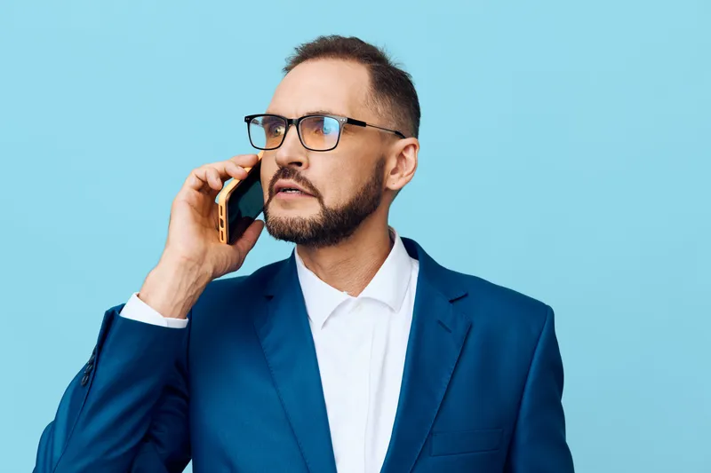 Confident business professional speaks on the phone, set against a bright colored backdrop. He conveys focus, determination, and calm authority in a modern work moment.
