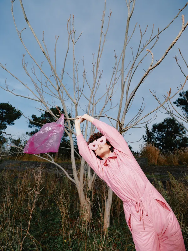 Dancing woman in pink scarf outdoors among leafless trees, capturing motion and carefree spring vibe in a vivid landscape with graceful movement and poetic energy