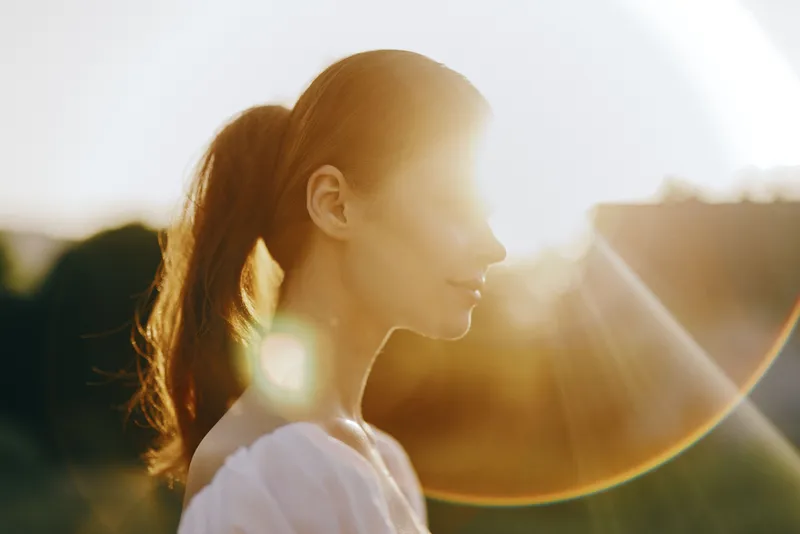 Profile of a young woman with long dark hair illuminated by the sunset, conveying tranquility and natural beauty in a warm, golden atmosphere