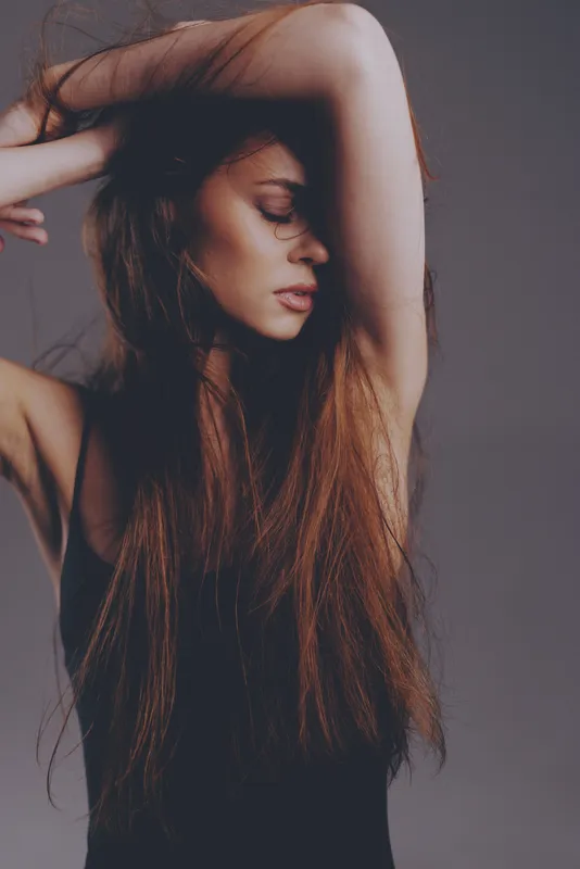 Woman with long hair posing with arm raised in soft moody lighting and neutral background