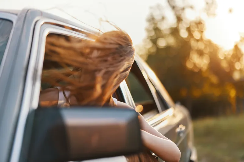 Young woman enjoying a summer road trip with windblown hair, celebrating freedom and adventure in a vibrant outdoor setting.