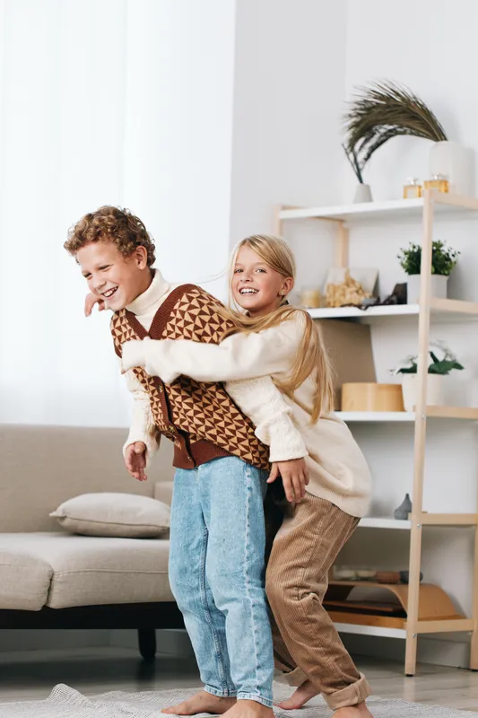Two smiling children playfully wrestle indoors on a cozy living room floor, capturing candid joy, movement, and carefree energy in a warm family setting.