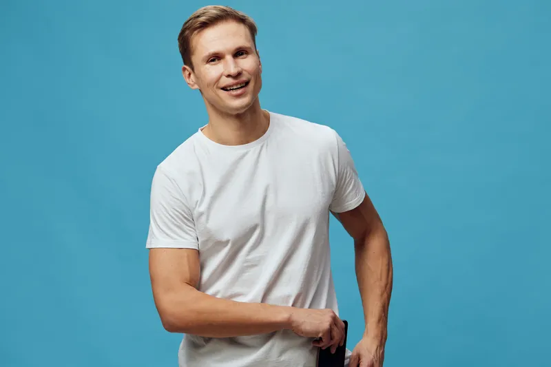 smiling happy young caucasian man wear white t-shirt hold phone pocket digital detox mental health concept isolated blue background studio portrait