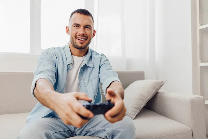 Smiling man engaging in gaming, enjoying a digital detox at home. Capturing the essence of modern relaxation amidst technology overload.