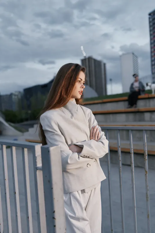 Confident woman in business attire standing outdoors, radiating professionalism amidst a modern cityscape with cloudy skies.