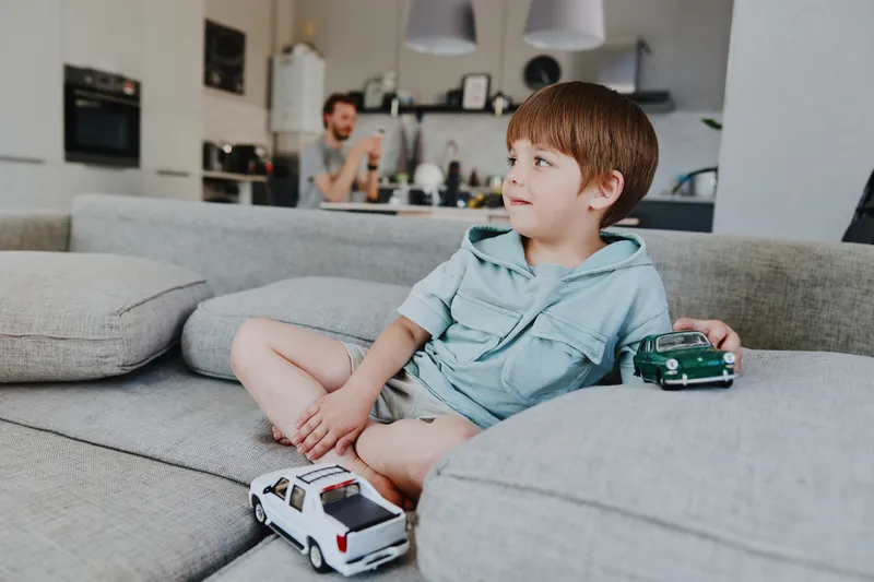 Happy boy playing with toy cars in a cozy living room, surrounded by soft furniture and minimalist decor, creating a cheerful atmosphere for playtime.