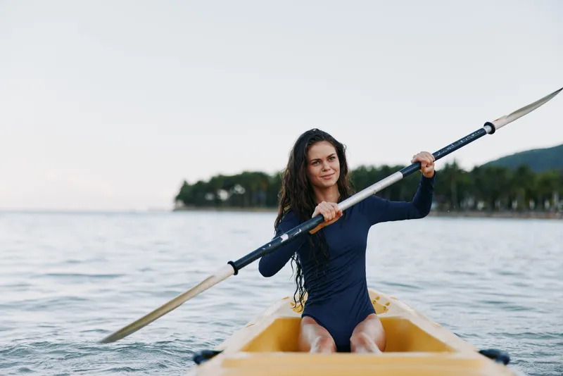 Young woman paddling kayak on calm water, outdoor activity, nature, summer, adventure, fitness