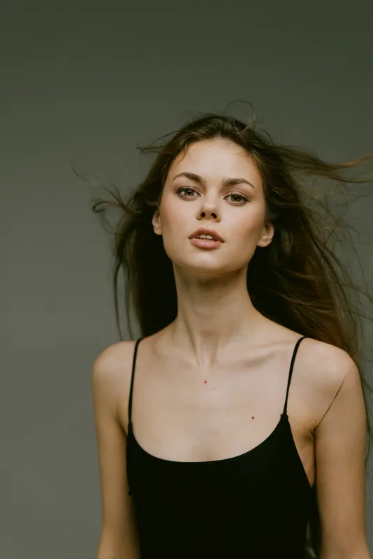 Young woman with flowing hair posing in a black tank top against a neutral background