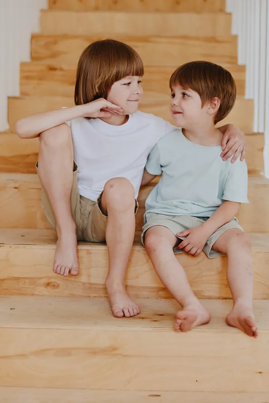Two cheerful boys sitting on wooden stairs share a playful moment, showcasing their friendship and innocence amidst a warm, natural setting.