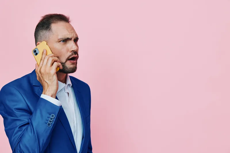A professional man on a pink isolated background talks on a yellow phone, conveying focus, confidence, and business presence with an urgent attitude.