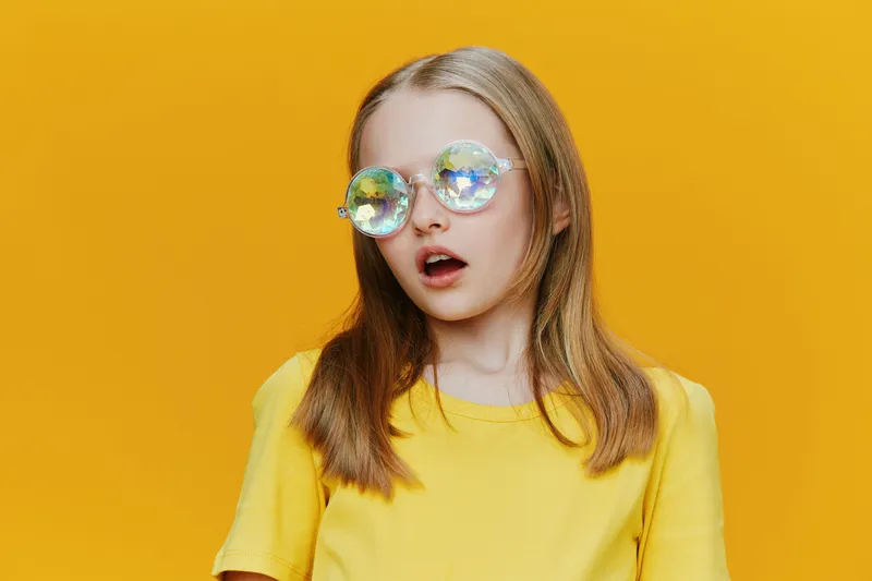 Young girl with stylish sunglasses, surprised expression, wearing a bright yellow t shirt, against a vibrant yellow background, perfect for summer concepts