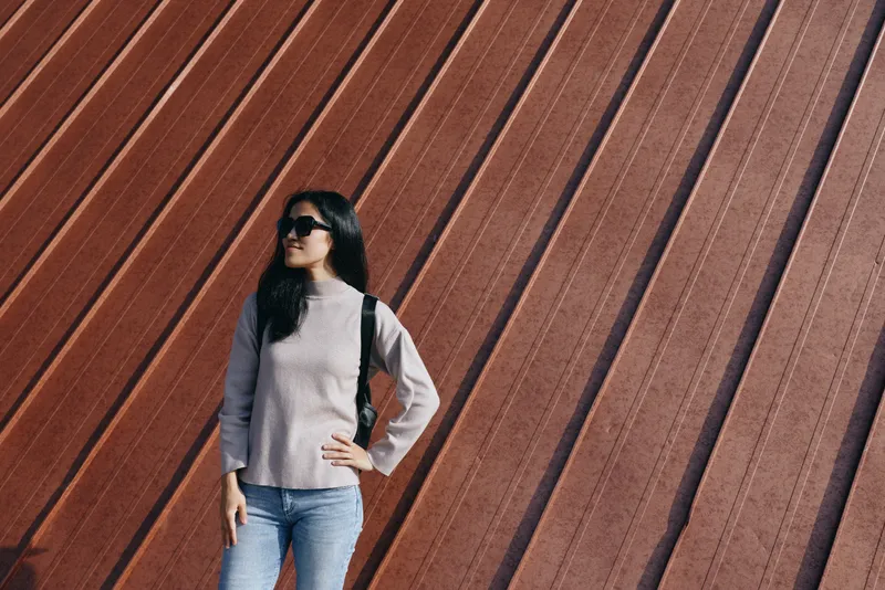 Woman with sunglasses in casual outfit posing against a diagonal rust wall, urban fashion scene highlighting confidence, street style and a poised stance for stock photography