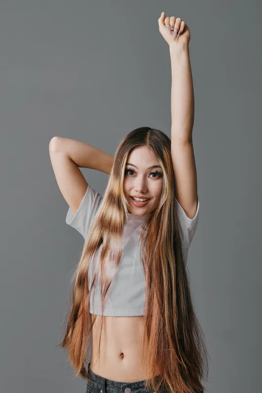 Young woman with long hair wearing casual t shirt raising arm and smiling on neutral background for beauty and confidence portrait.