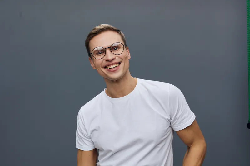 Smiling young caucasian man wearing round glasses white t-shirt look camera happy cheerful joyful pose studio portrait digital nomad remote work concept