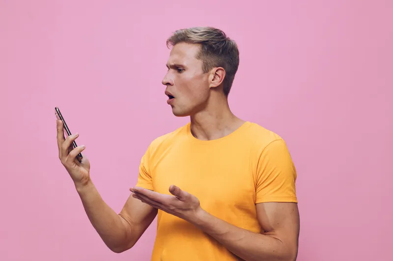 surprised man in yellow t-shirt using smartphone voice assistant pink background casual lifestyle concept digital assistant technology