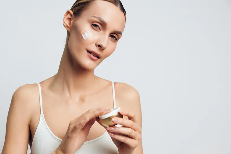 Woman skincare beauty portrait, applying cream to face with applicator, calm expression, studio background, daily self care treatment concept for dermatology and healthy glow