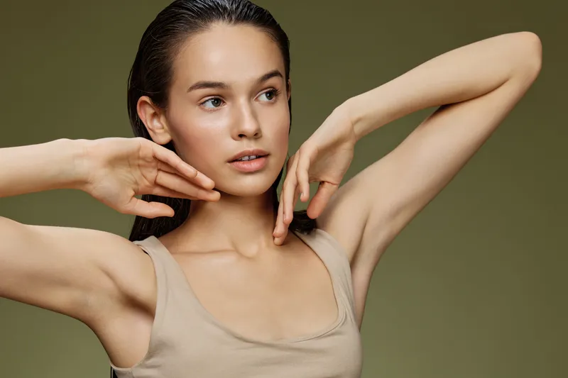 A young model with a natural look posing against a soft green background, showcasing a radient expression and healthy skin, perfect for beauty and wellness themes