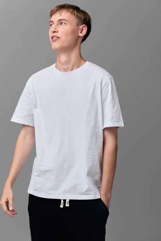 Man wearing a plain white tshirt in a minimal studio setup, relaxed pose with hands in pockets, focused expression, simple fashion and casual style for lifestyle clothing showcase