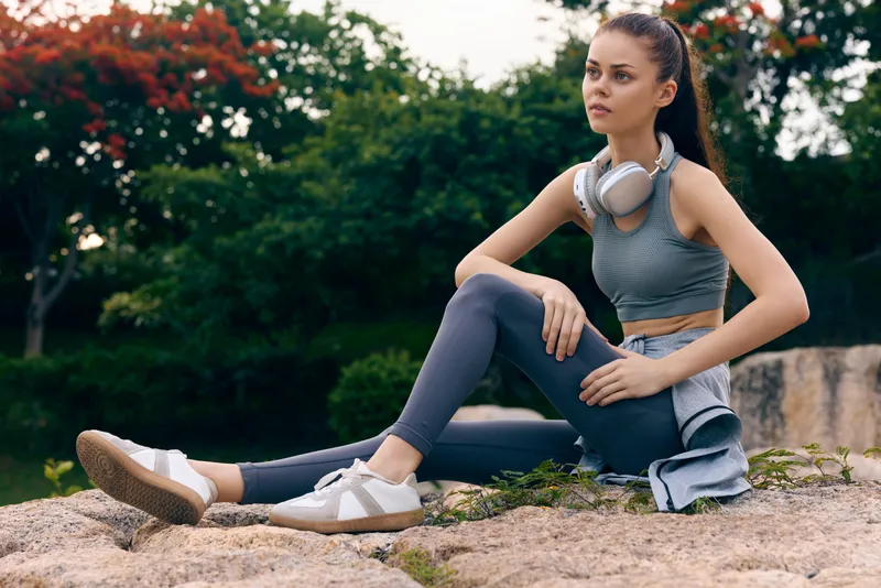 Young athletic woman in casual sportswear relaxing outdoors, showcasing fitness lifestyle, serenity, and natural beauty in a vibrant park setting